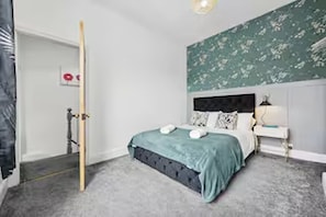 Quarto com cama, mesa de cabeceira e parede com padrão floral.