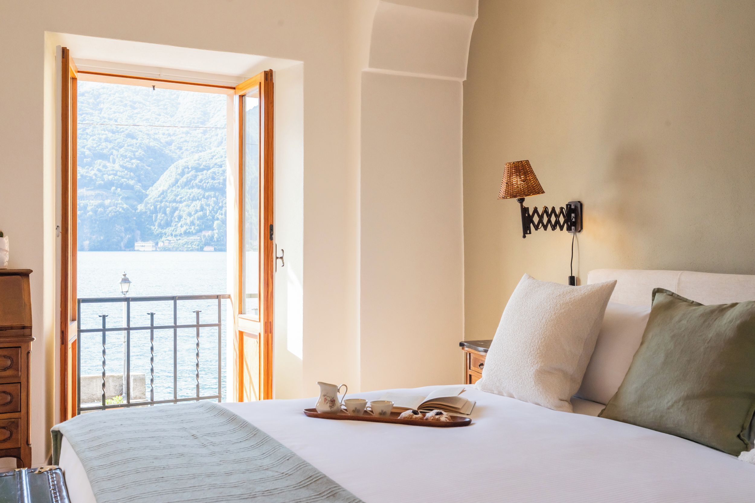 A bedroom with a bed, a bedside table, a lamp, and a view of a body of water through an open door.