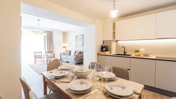 Ein Essbereich mit Tisch für vier Personen, eine Küche mit modernen Geräten und ein Wohnbereich mit Sofa und Gemälde.