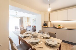 Ein Essbereich mit Tisch für vier Personen, eine Küche mit modernen Geräten und ein Wohnbereich mit Sofa und Gemälde.