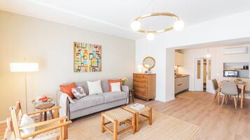 Ein modernes Wohnzimmer mit einer Couch, Couchtisch und Sesseln, eine Küchenzeile mit Esstisch und ein Essbereich mit einem Stuhl.
