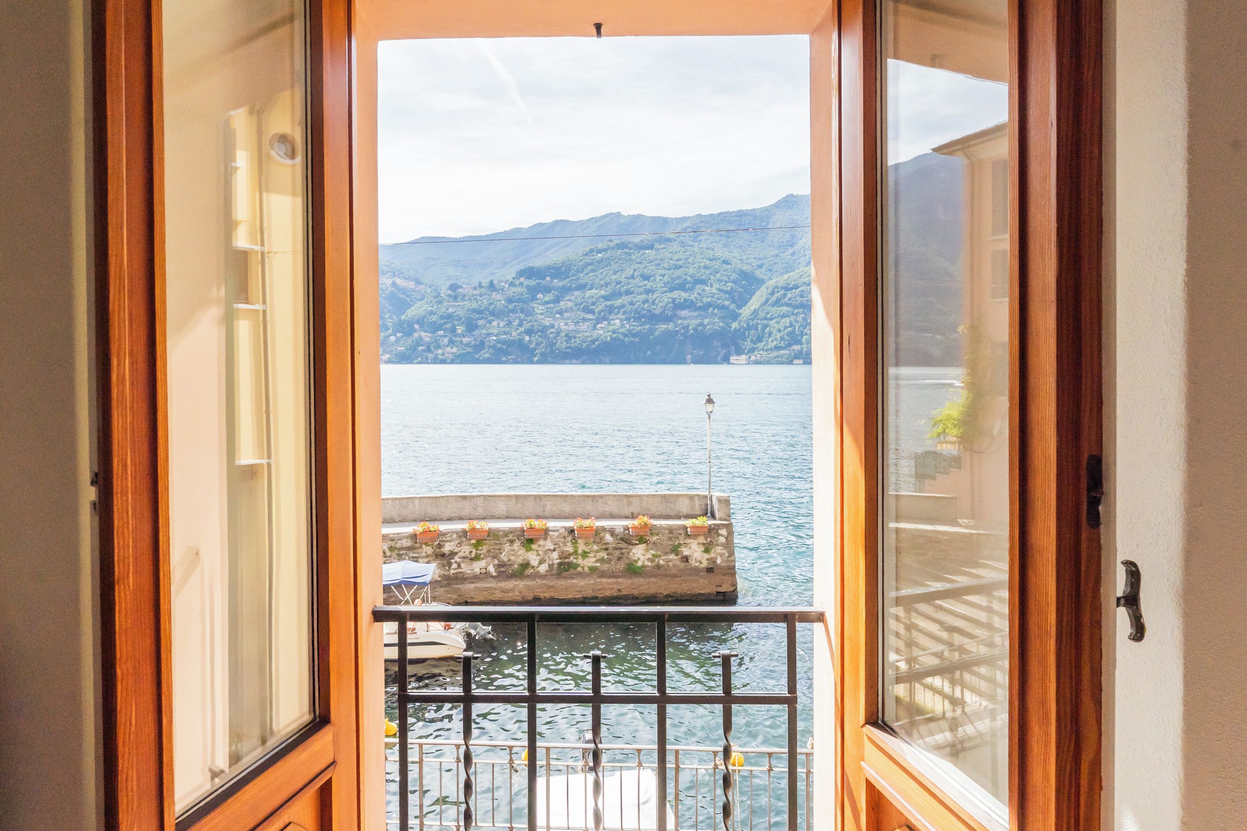 Blick von einem Balkon mit Geländer auf ein Gewässer und eine gebirgige Landschaft.