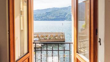 Blick von einem Balkon mit Geländer auf ein Gewässer und eine gebirgige Landschaft.