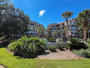 A multi-story hotel with a pool, surrounded by lush greenery and palm trees. - Luxury 2 bed 2 ba Penthouse - Shelter Cove Marina Views (Hilton Head Island)