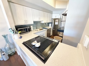 A modern kitchen with white cabinets, a black induction cooktop, a stainless steel refrigerator, and a microwave. - Luxury 2 bed 2 ba Penthouse - Shelter Cove Marina Views (Hilton Head Island)