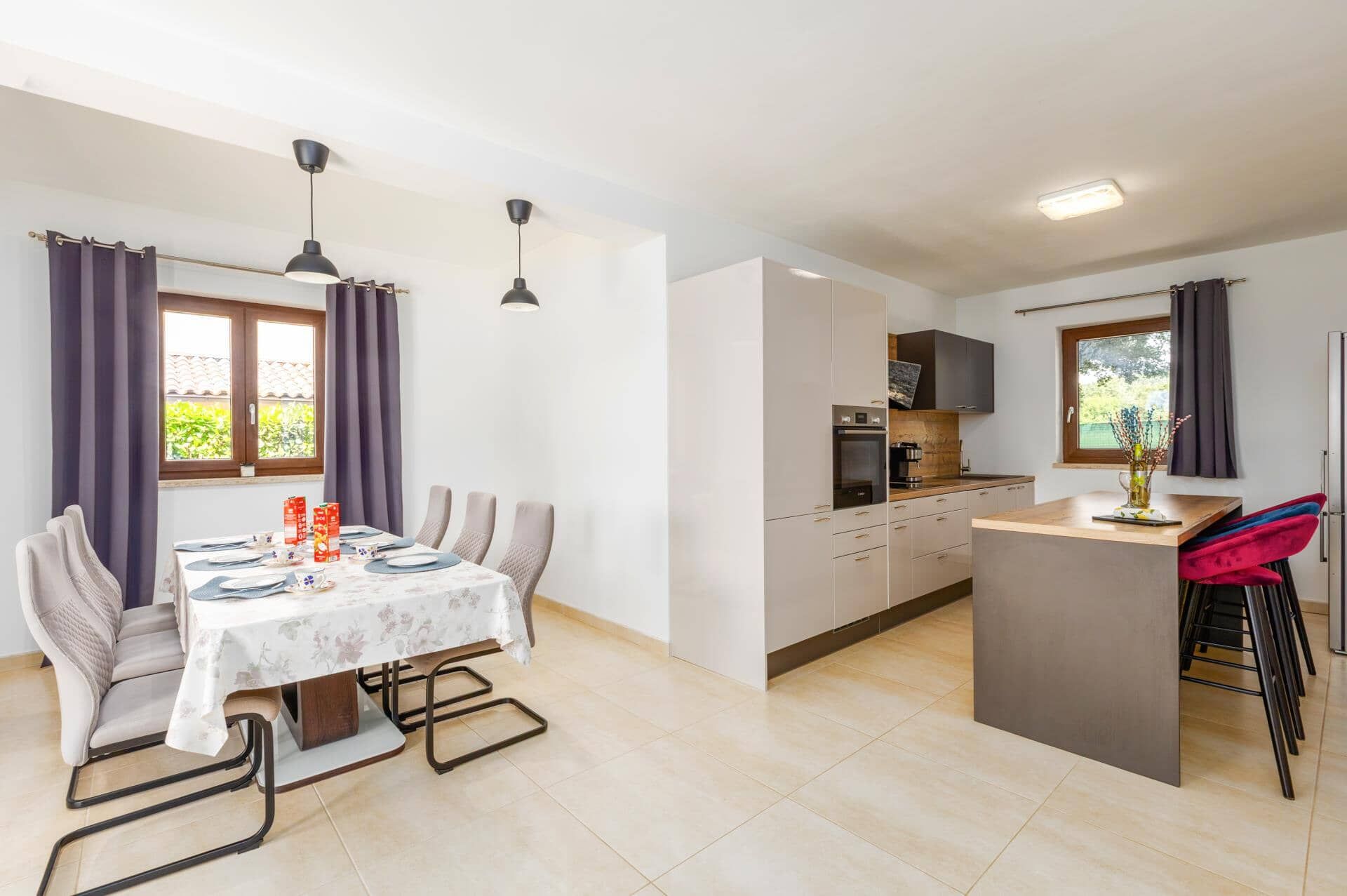 A modern kitchen with a dining area, featuring a table set for four, a built-in oven, and a small island with seating.