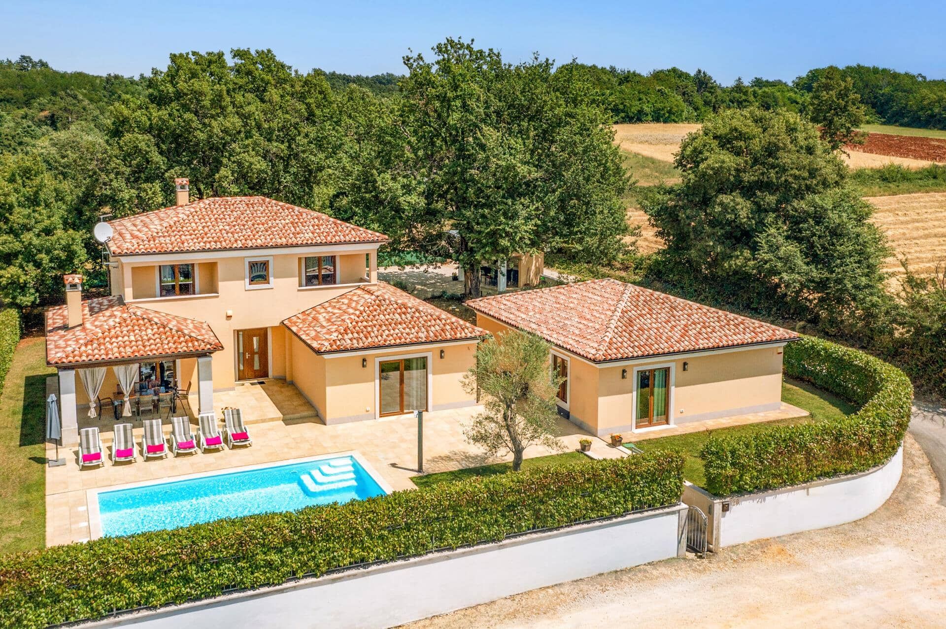 Una casa de dos pisos con piscina, rodeada de vegetación y colinas.