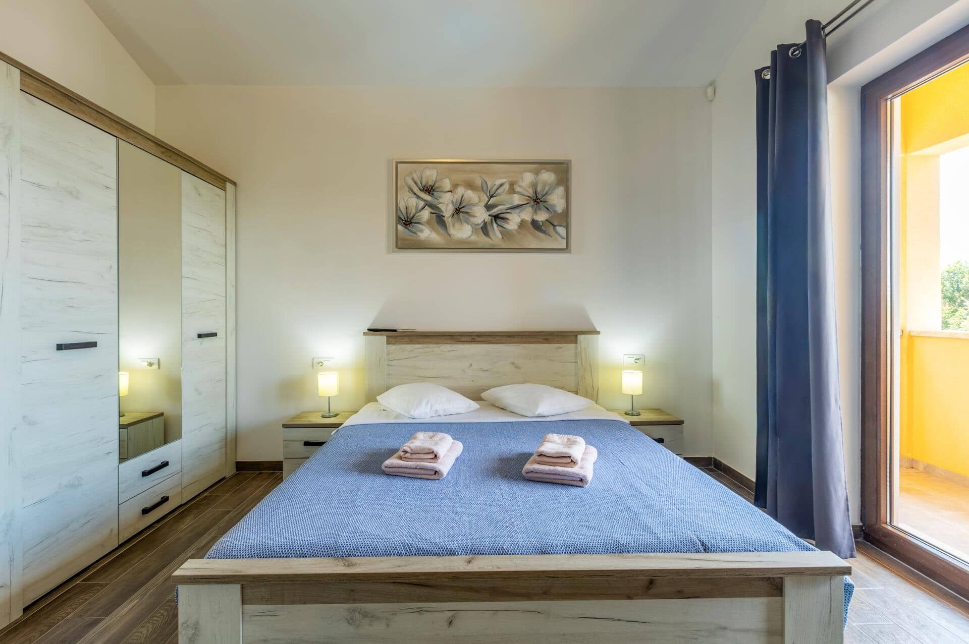 Une chambre à coucher avec un lit, des lampes de chevet, un tableau et une vue par la fenêtre.