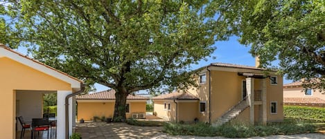 Um pátio com um edifício, uma árvore e área de estar com cadeiras e uma mesa.