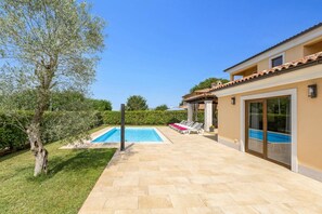 Ein Poolbereich mit gefliestem Deck, einer Pergola und Liegestühlen.