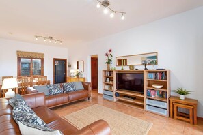 Ein Wohnzimmer mit braunem Ledersofa, einem Fernseher, Holzregalen und einem Essbereich mit Stühlen und einem Tisch.
