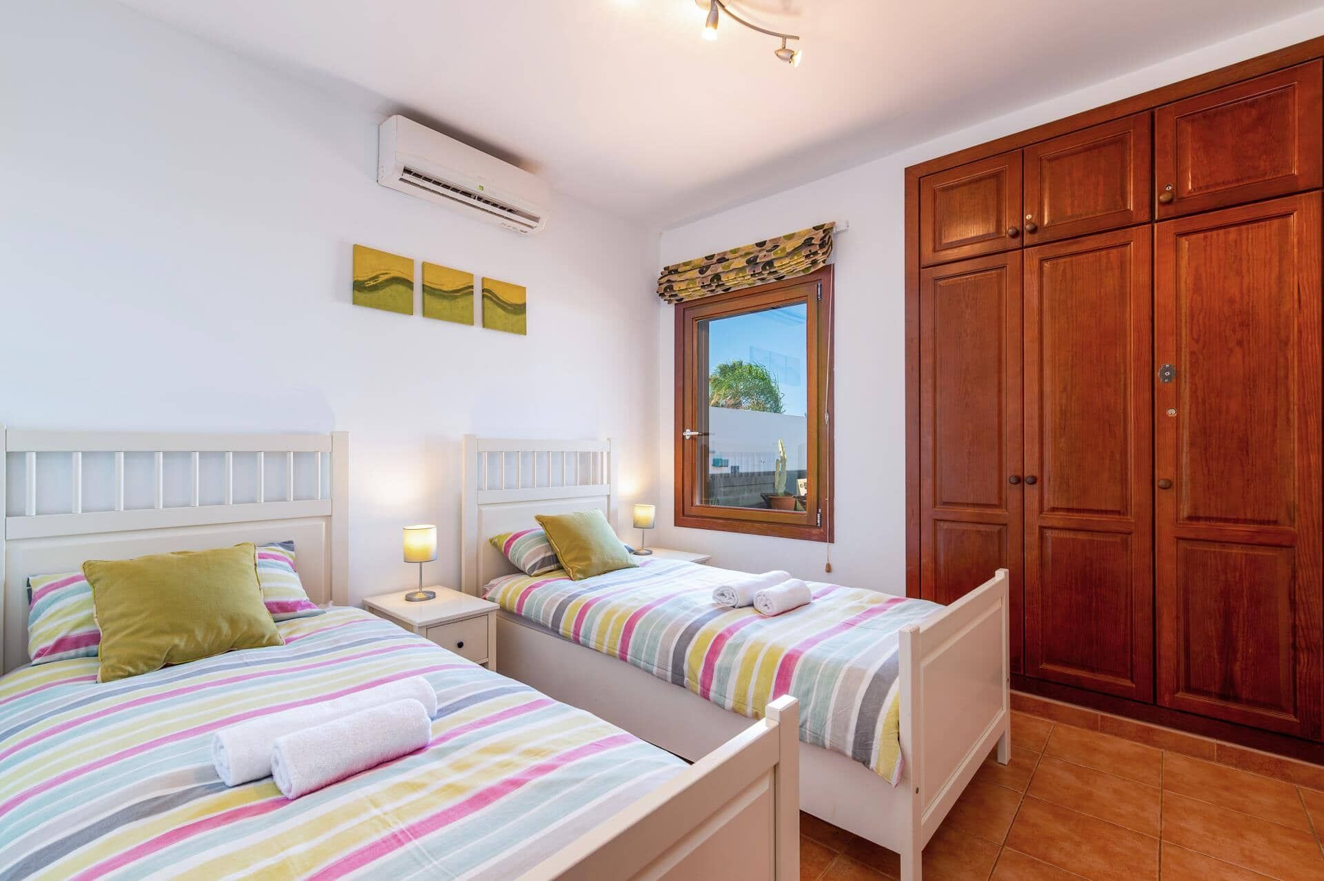 A bedroom with two beds, a wardrobe, an air conditioning unit, and a window with a view.