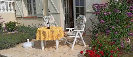 An outdoor patio with a table set for two, a bottle of wine, and two chairs with floral upholstery.