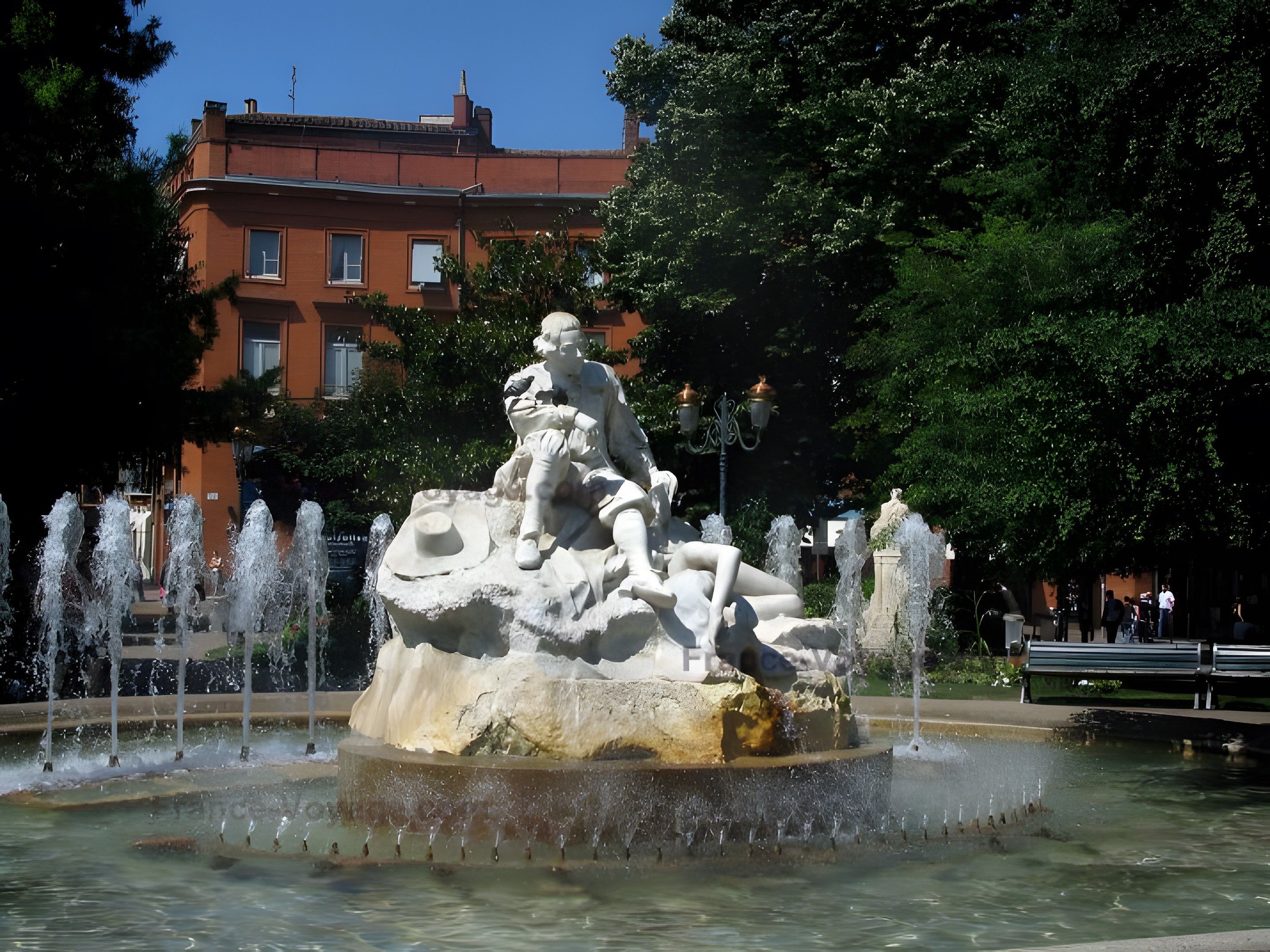 A fountain with multiple water jets and a statue of a seated figure.