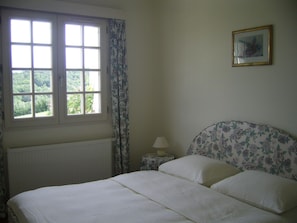 A bedroom with a bed, a window, a nightstand with a lamp, and a floral-patterned headboard. - Holiday Home 'La Source' with WiFi and Pyrenees View (Puymaurin)