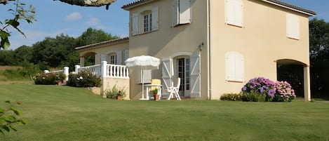 A two-story house with a balcony, a white umbrella, and a chair.