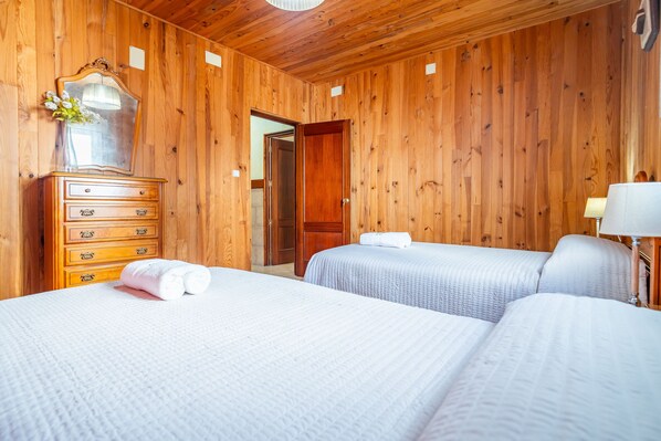 A wooden-paneled room with two beds, a dresser, a mirror, and a door leading to another room.