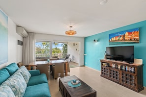 A living room with a sofa, a coffee table, a TV, and a bookshelf. - Tropical Paradise at Blue Bay | Pool & Beach Access (Willemstad)