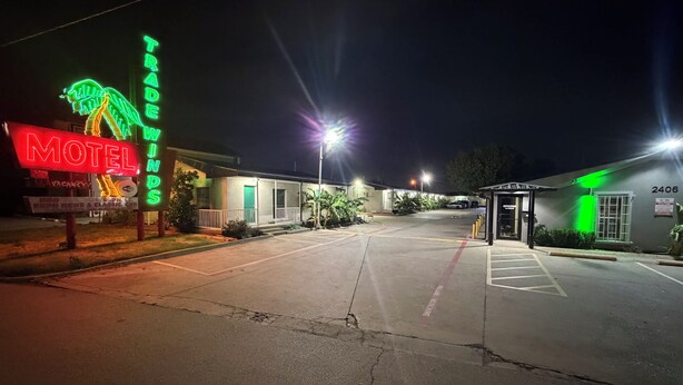 Un motel con un letrero de neón, un estacionamiento y la entrada al edificio.