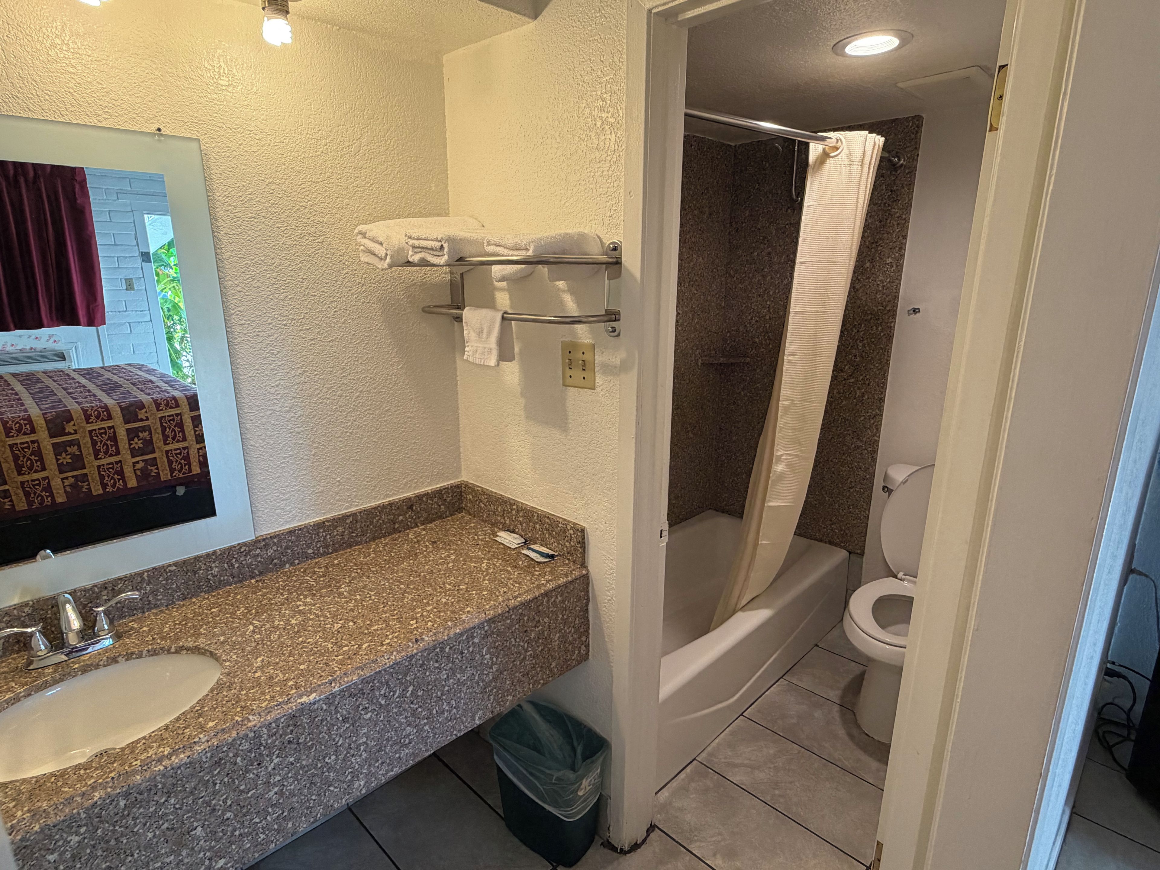 Une salle de bain avec un lavabo doté d’un plan de travail en granit, un porte-serviettes et un rideau de douche.