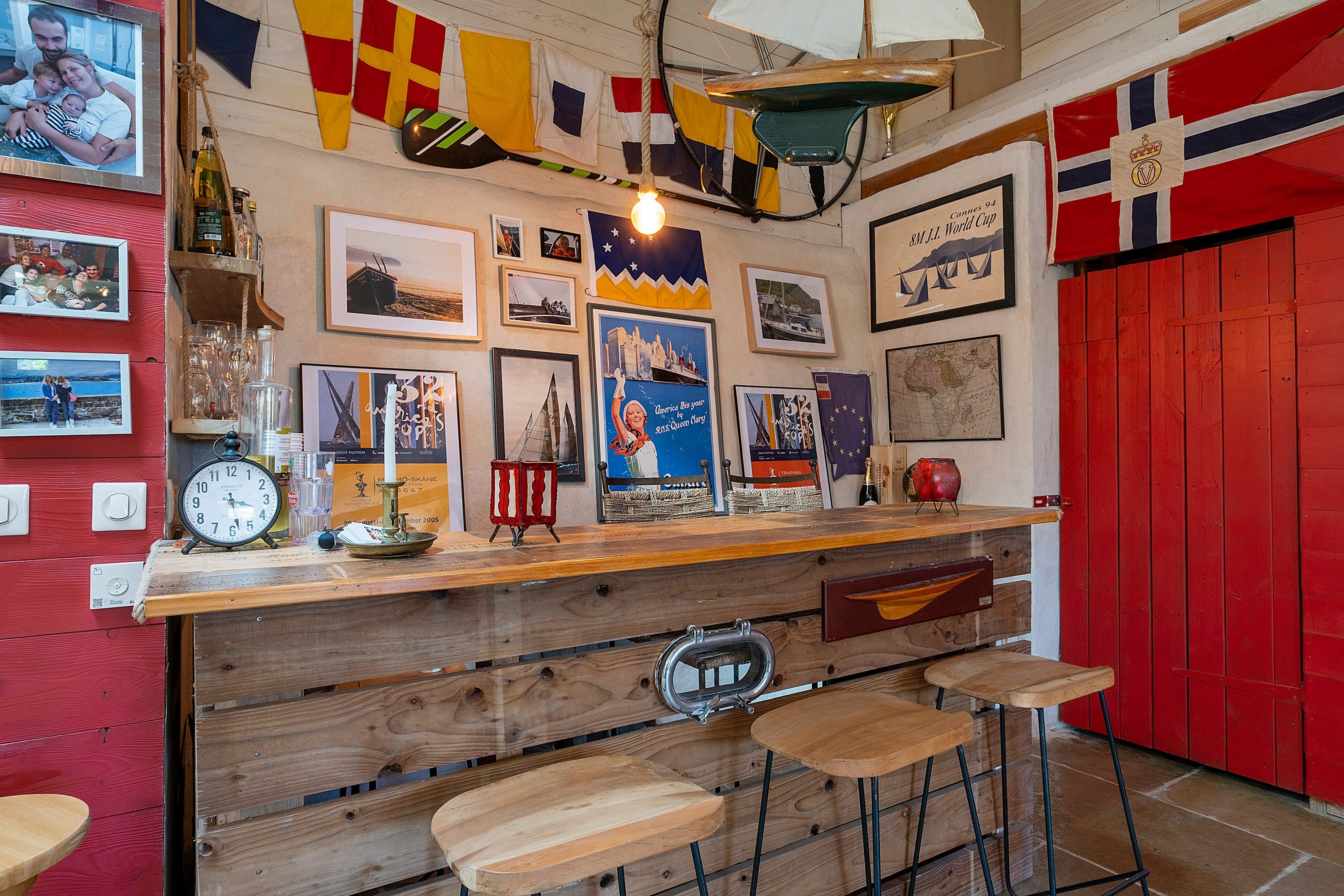 A bar area with wooden stools, a clock, and various framed pictures on the wall.