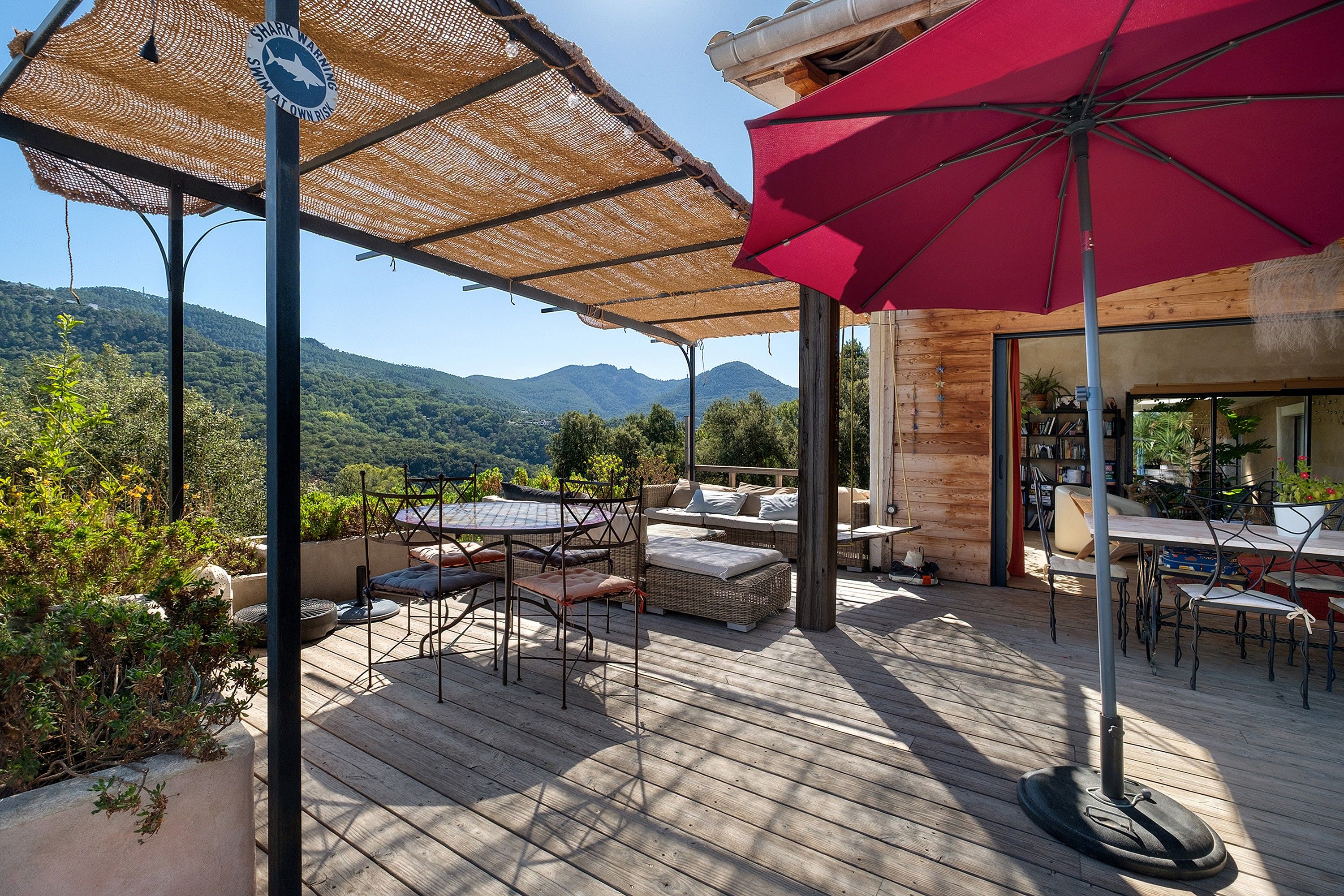 Un patio al aire libre con suelo de madera, mobiliario de mimbre y un paraguas rojo.