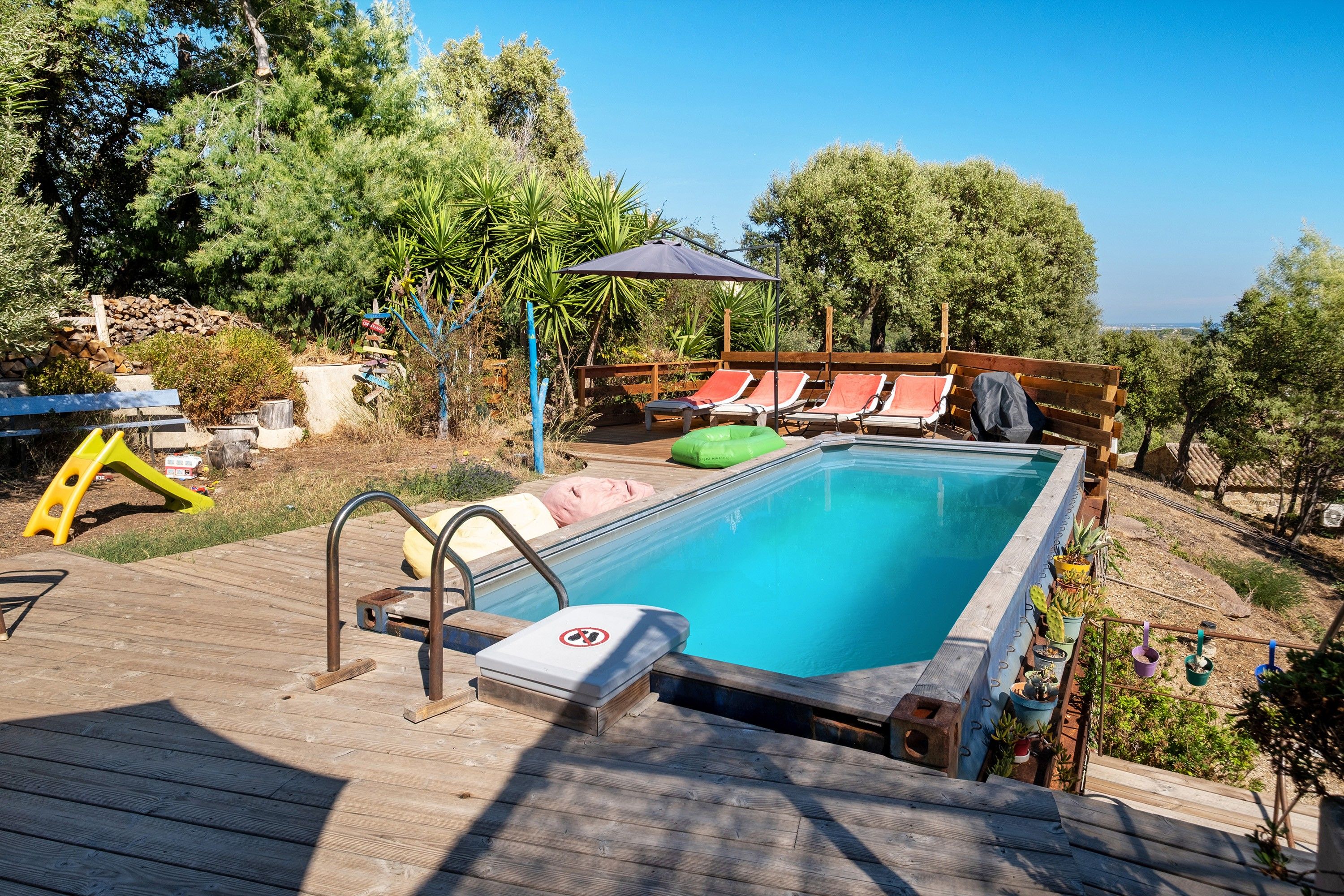 Une piscine avec une terrasse en bois, des chaises longues et un panneau indiquant qu’il est interdit de se baigner.