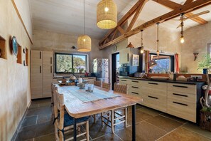 A rustic kitchen with a wooden table, hanging lights, and a view to the outside. - Villa 'Sawubona' with Mountain View, Private Terrace and Wi-Fi (Les Adrets-de-l'Estérel)