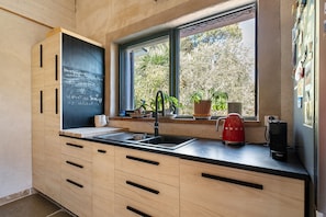 A modern kitchen with a blackboard, wooden cabinets, a sink, and a window with plants. - Villa 'Sawubona' with Mountain View, Private Terrace and Wi-Fi (Les Adrets-de-l'Estérel)