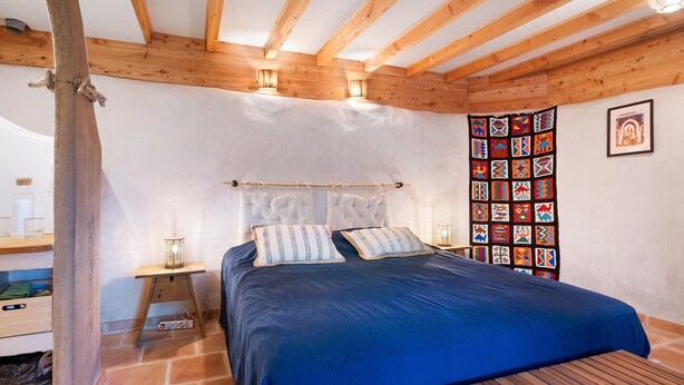 Une chambre à coucher avec un lit, des poutres en bois, une tapisserie murale et une table de chevet avec une lampe.