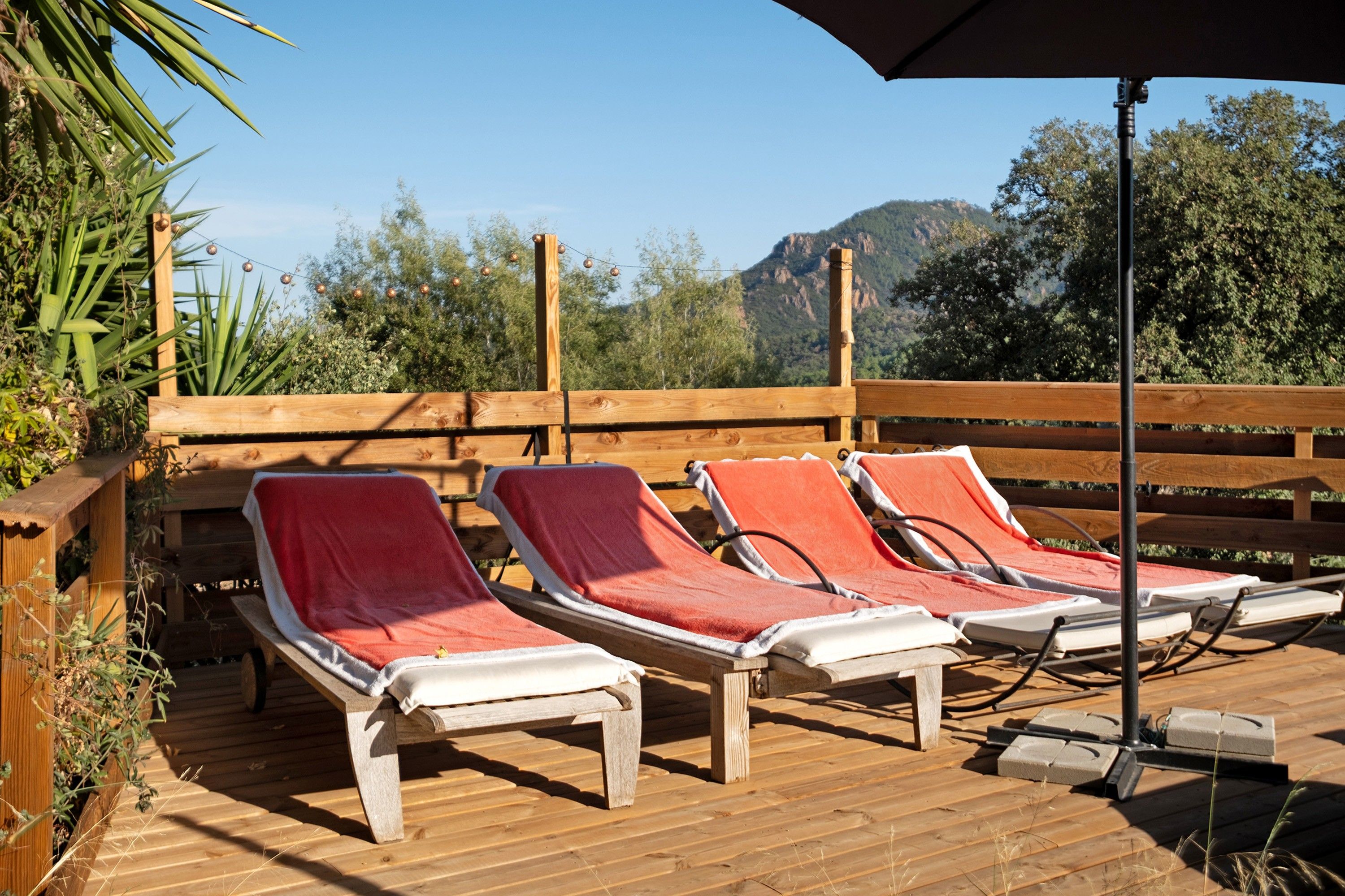 A wooden deck with lounge chairs and a table, overlooking a mountainous landscape.
