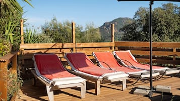 A wooden deck with lounge chairs and a table, overlooking a mountainous landscape.