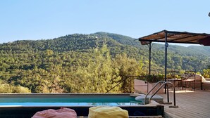 Une terrasse en bois avec une piscine, deux fauteuils de relaxation et une vue sur une montagne boisée.