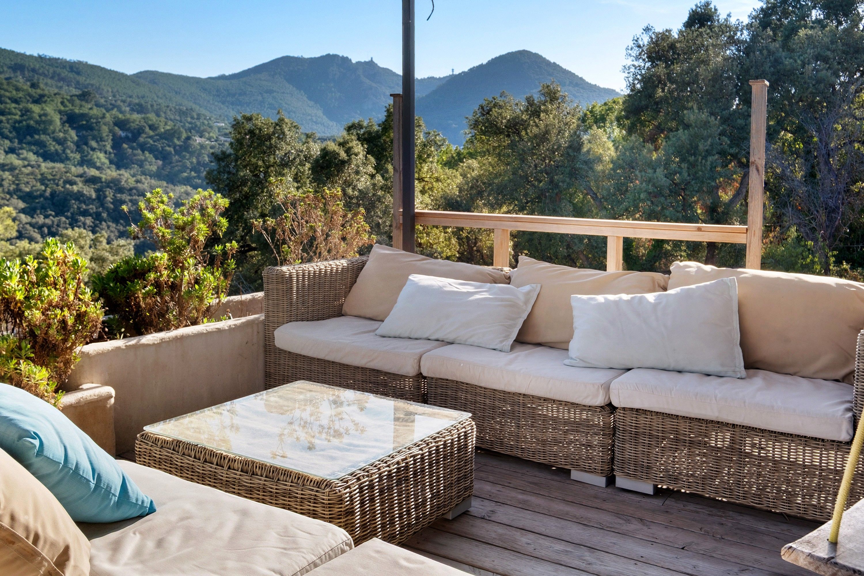 Un canapé en osier avec des coussins, placé sur une terrasse extérieure offrant une vue sur la montagne.