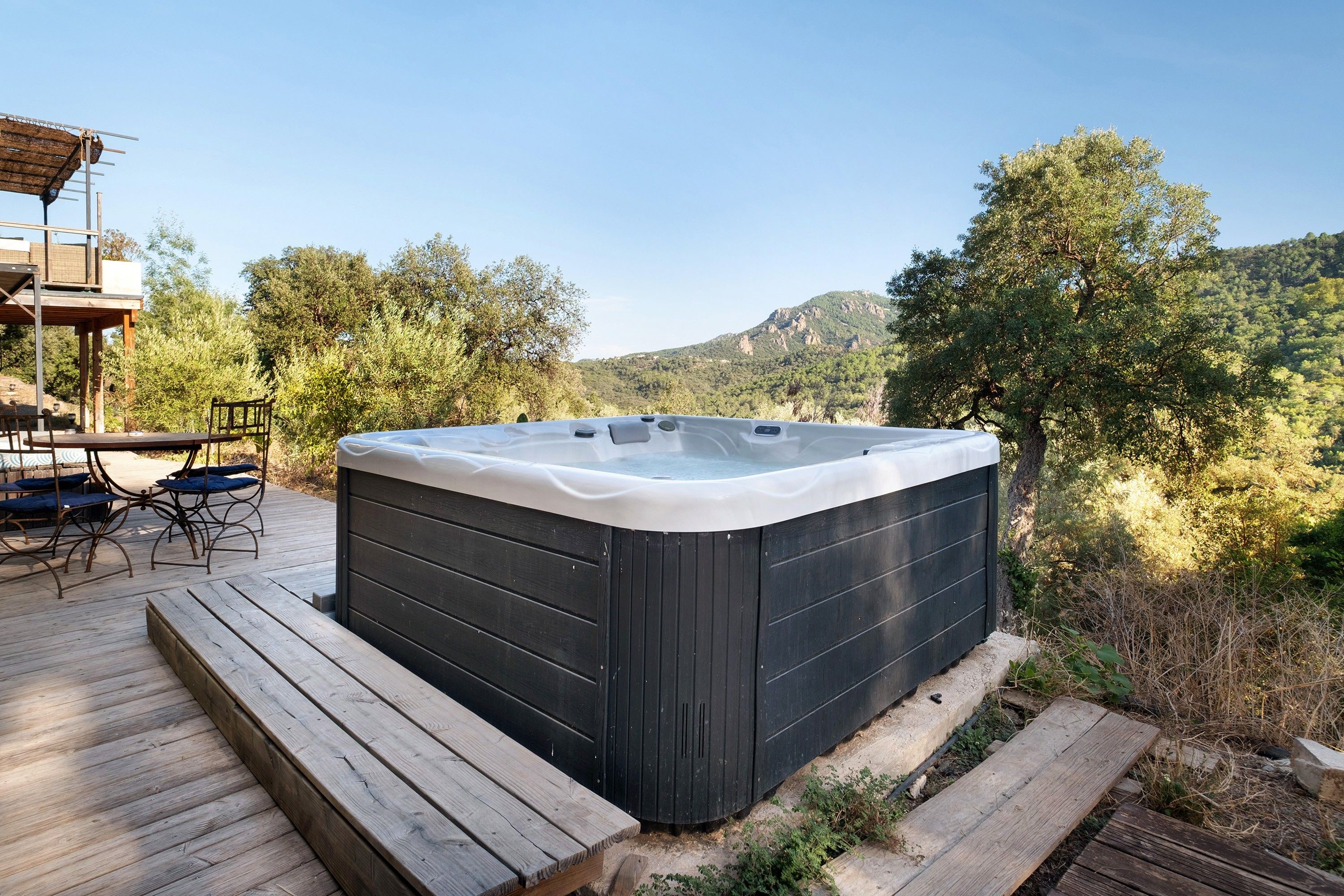 Un bain à remous sur une terrasse en bois, avec vue sur une montagne et des arbres.