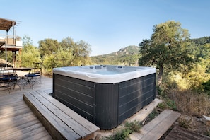 A hot tub on a wooden deck with a view of a mountain and trees.