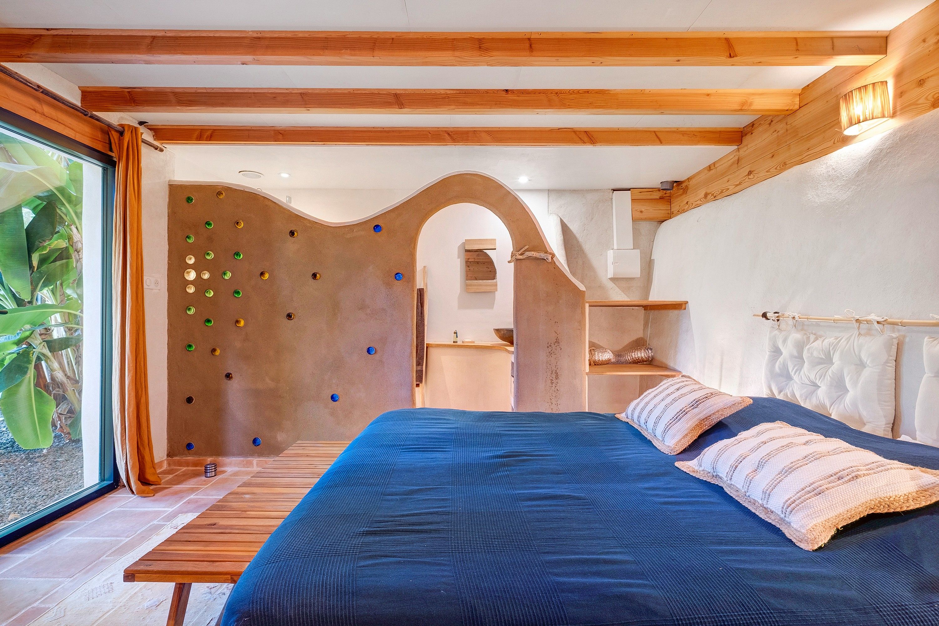 Une chambre avec un lit, des poutres en bois, un mur d’escalade et une vue sur la verdure.