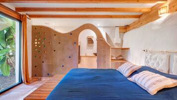 Une chambre avec un lit, des poutres en bois, un mur d’escalade et une vue sur la verdure.