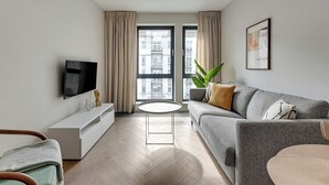 A modern living room with a flat-screen TV, a sofa, a coffee table, and a potted plant. - Bank Polski City Center with Parking (Gdynia)