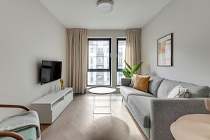 Ein modernes Wohnzimmer mit Flachbildfernseher, einer Couch, einem Couchtisch und einer Topfpflanze.