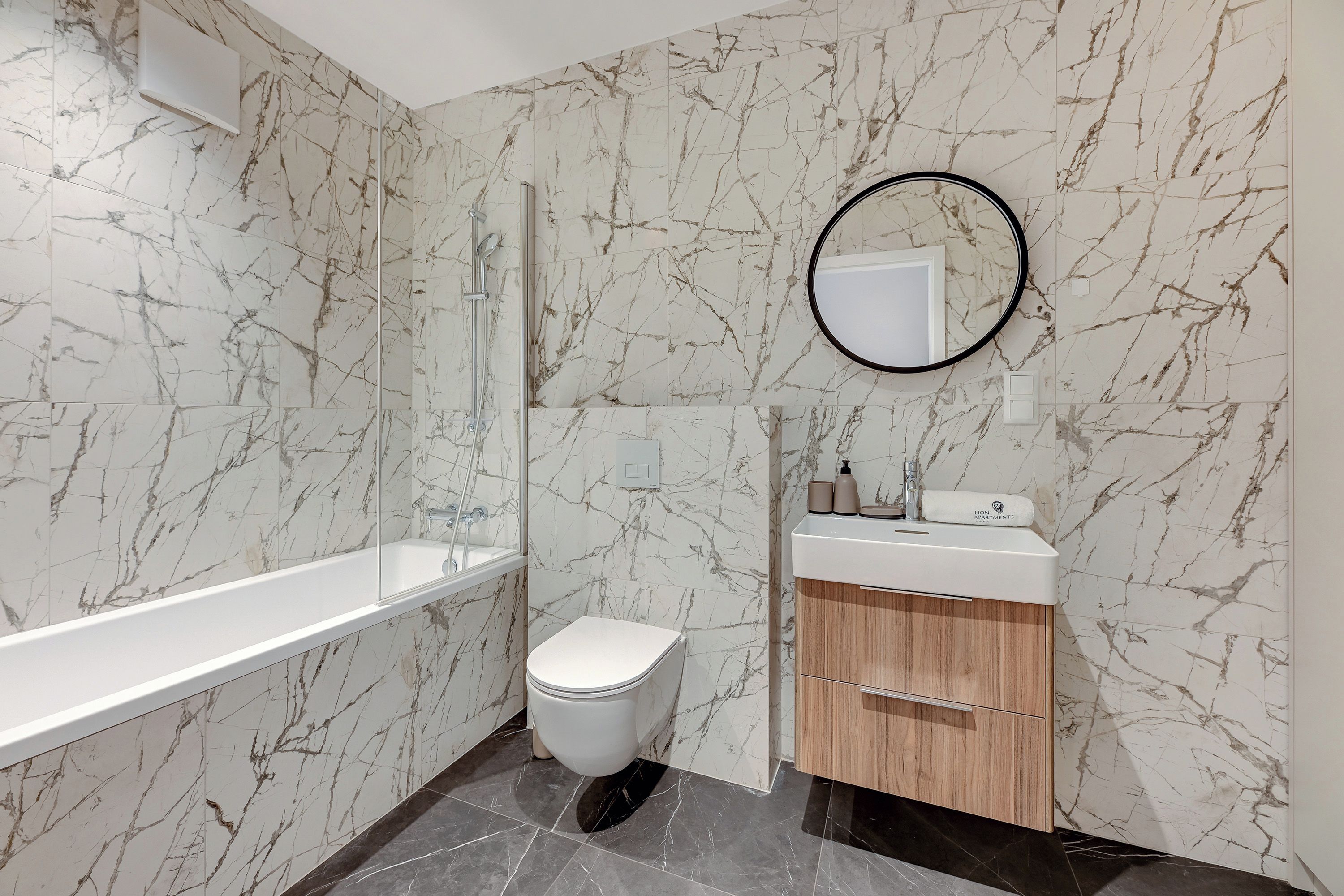 A bathroom with a marble wall, a bathtub, a toilet, a sink with a mirror, and a vanity cabinet.