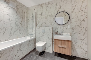 Ein Badezimmer mit Marmorwand, einer Badewanne, einer Toilette, einem Waschbecken mit Spiegel und einem Schminktisch.