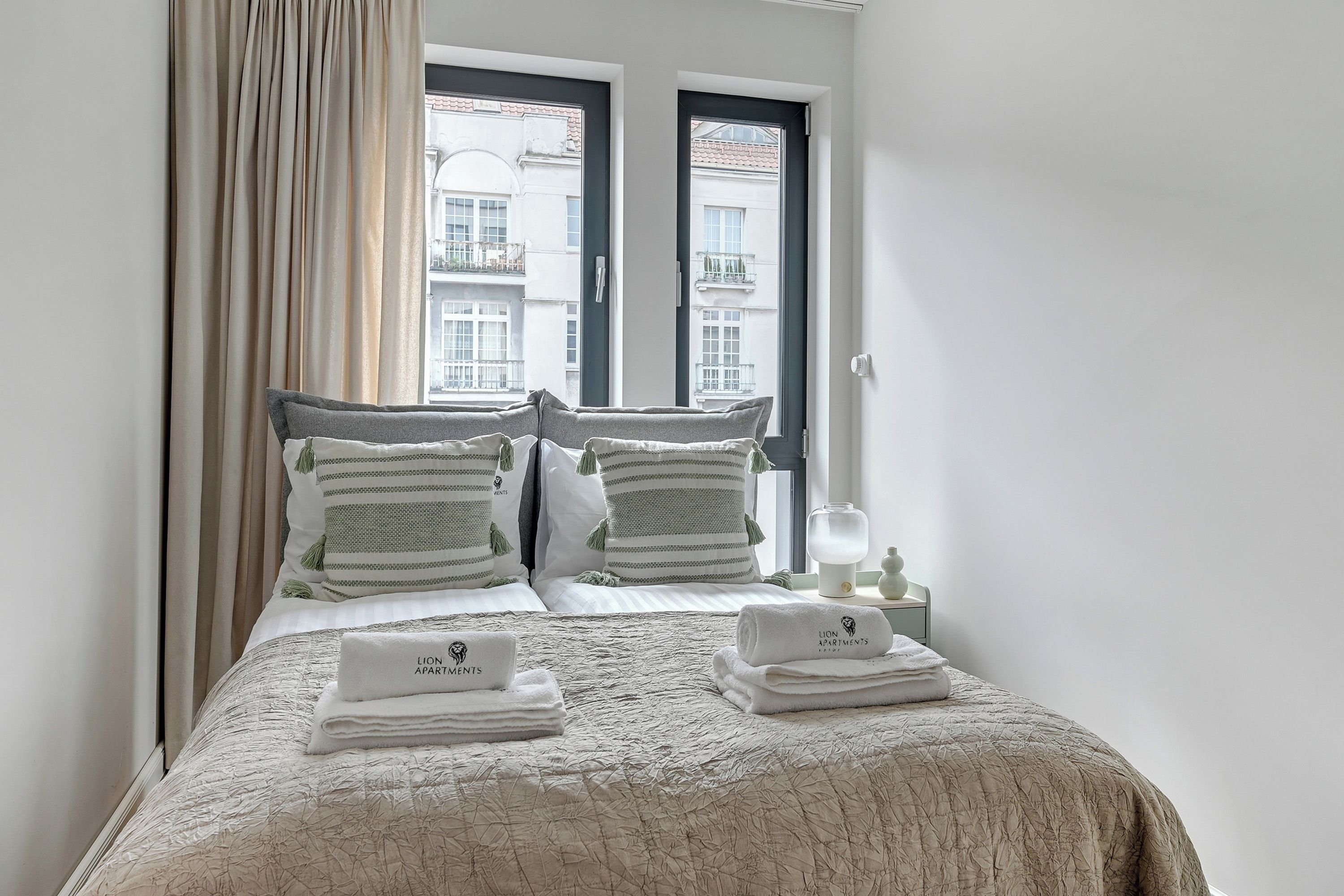 A neatly made bed with a textured blanket, two pillows with tassels, and a set of folded towels on a bedside table.