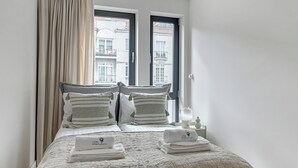 A neatly made bed with a textured blanket, two pillows with tassels, and a set of folded towels on a bedside table. - Bank Polski City Center with Parking (Gdynia)