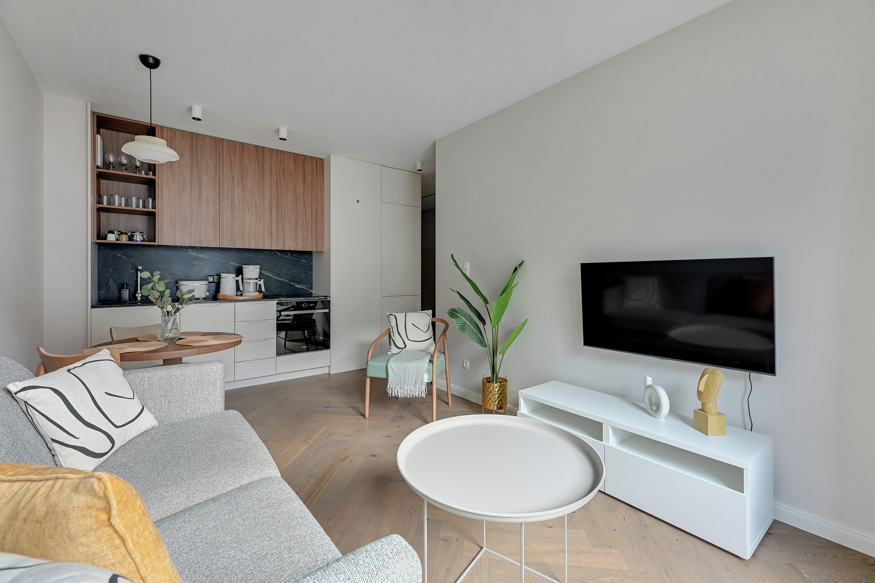 A modern living room with a grey sofa, a white coffee table, and a flat-screen TV on a white stand.
