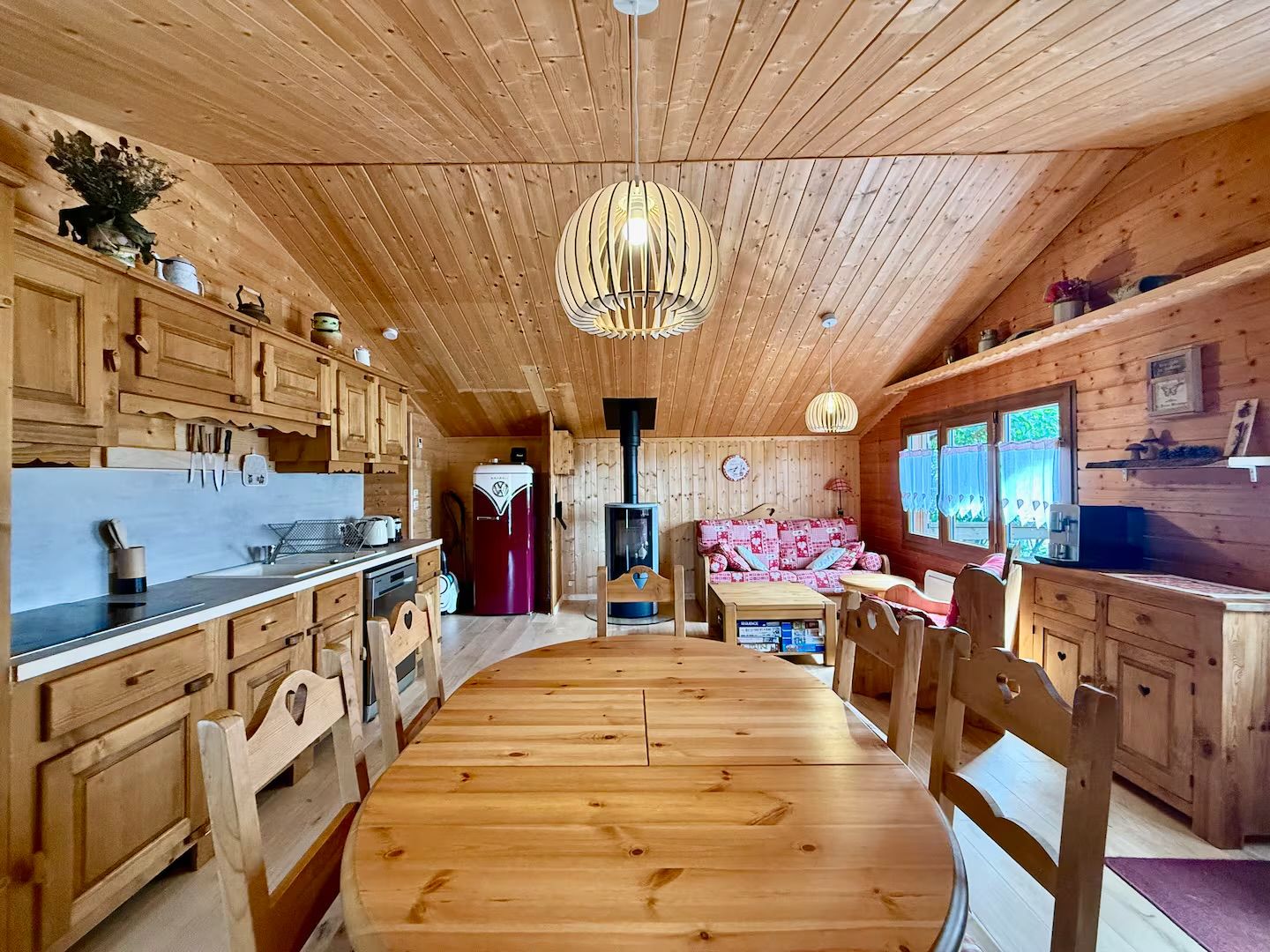 Ein Interieur einer Holzhütte mit einem zentralen Esstisch, Holzschränken und einer Hängelampe.