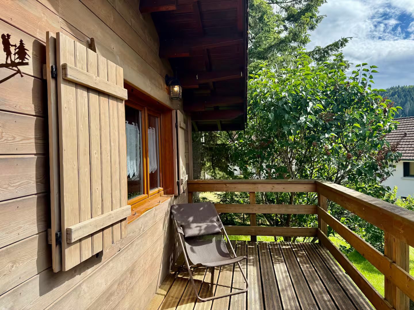 A wooden cabin with a balcony, a chair, and a window with shutters.