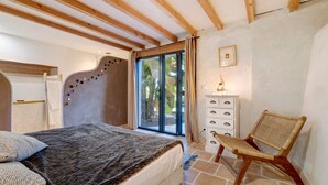 Un dormitorio con cama, una silla, cómoda y ventana con cortinas.