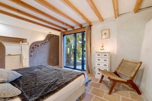 Ein Schlafzimmer mit einem Bett, einem Sessel, einer Kommode und einem Fenster mit Vorhängen.