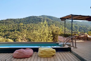 Eine Holzterrasse mit Pool, zwei Sitzsäcken und Blick auf einen bewaldeten Berg.